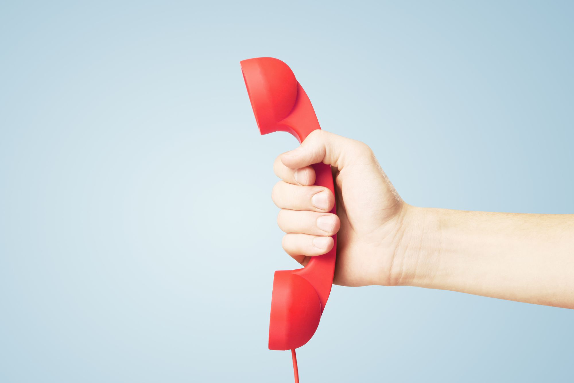 A hand holds an old-fashioned red telephone in front of a blue background to represent answering phone leads.