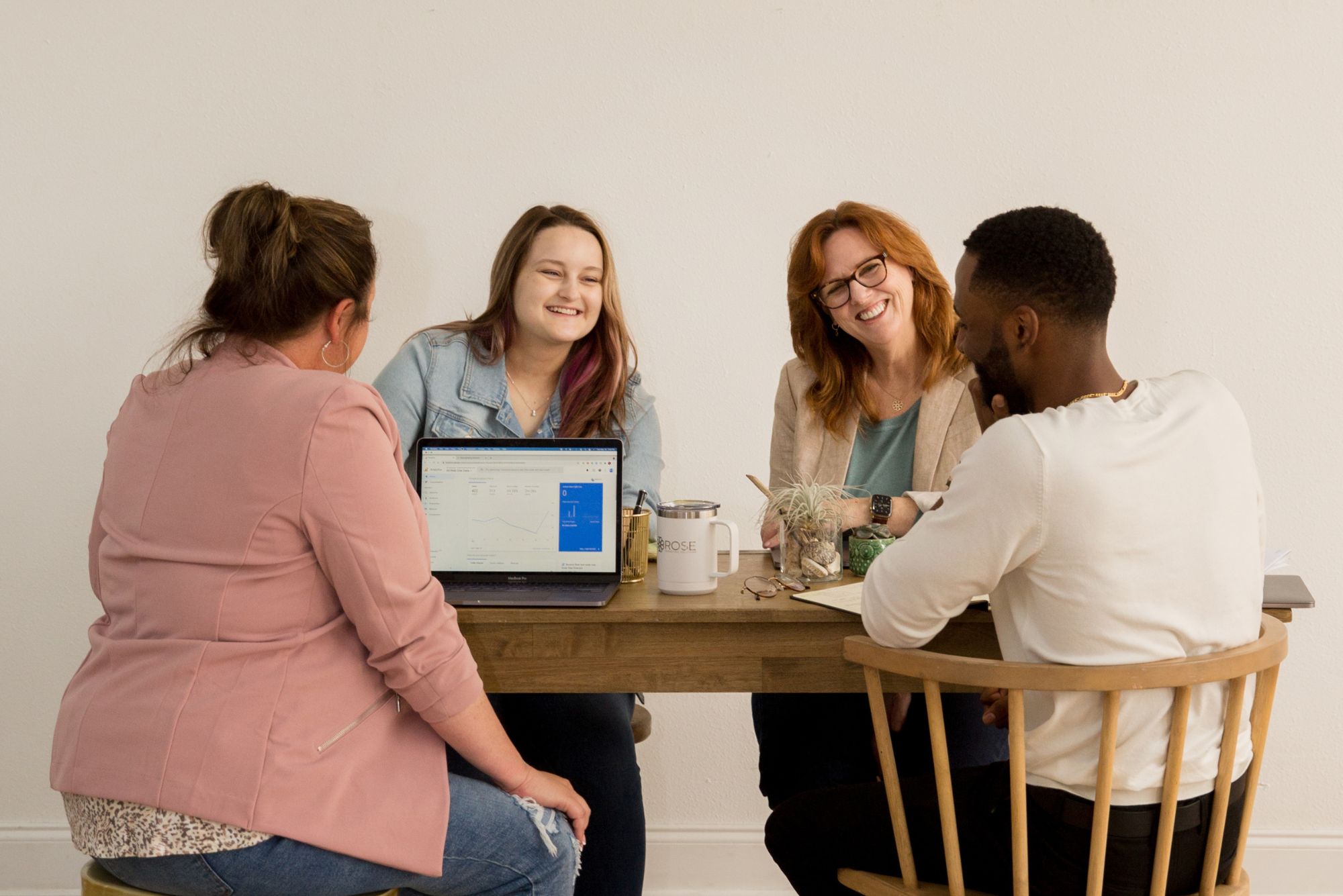 Four childcare center owners sit around a table and laptop sharing childcare staffing tips.