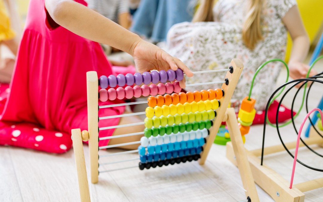 A young child’s hand moves purple and pink pieces to the side on a rainbow-colored toy abacus.