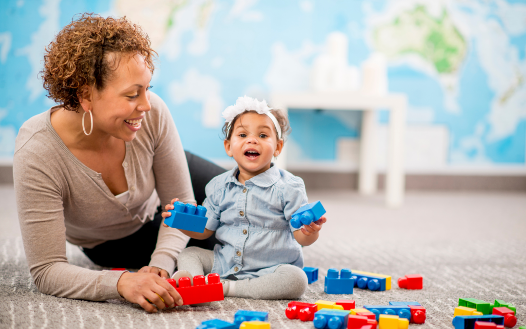 A mom and baby smile while playing on the floor of a childcare center they are touring.